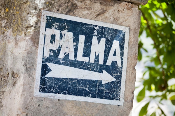 Den här vägen till Palma. Palma de Mallorca är huvudstaden på Balearerna i södra Mallorca. Detta gamla, målade och nödställda vägskylt på en stenmur, överhängt av buskar, återspeglar en svunnen tid.