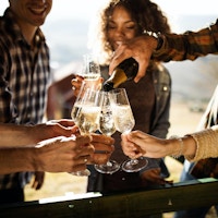 Närbild på lyckliga vänner som har kul medan du dricker champagne på ett terrassparti. En av dem häller.