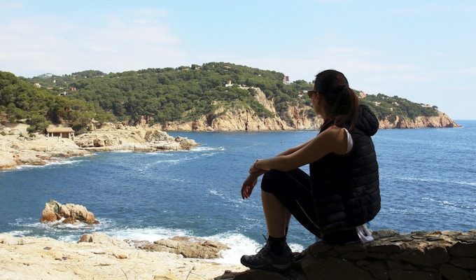 Den unga kvinnan vilar framför Medelhavet under en vårslinga mellan byarna Tamariu och Calella de Palafurgell, Costa Brava, Katalonien, Spanien.