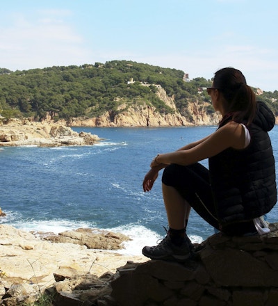 Den unga kvinnan vilar framför Medelhavet under en vårslinga mellan byarna Tamariu och Calella de Palafurgell, Costa Brava, Katalonien, Spanien.