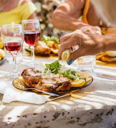 Lady njuter av sin mat serveras med en halv platta kött och den andra halvan sallad. Hon sitter vid bordet med sina vänner i restaurangen på sin semester.