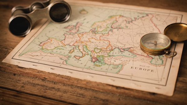 "Färgbild av en gammal karta över Europa, från 1800-talet, med kikare och kompass, på träbakgrund. Karta är från en gammal geografibok med 1870 upphovsrätt."