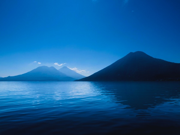 Djupblå: Lake Atitlan, Guatemala silhuett av vulkaner på blå sjö