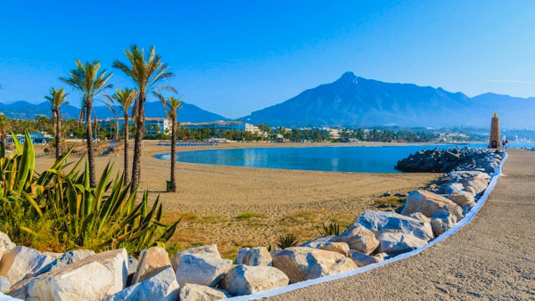 Blå himmel, fin sandstrand, palmer, berg i bakgrunden, Puerto Banus, Marbella, Spanien