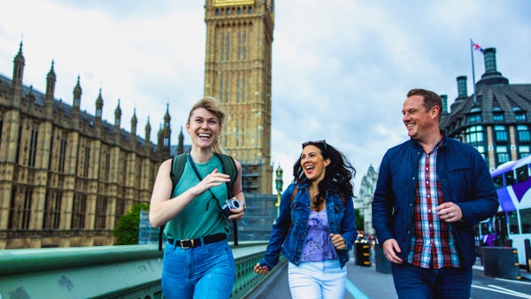 Långbenta vuxna kaukasiska vänner har roligt medan de utforskar Londons landmärken. De går förbi Palace of Westminster. De tittar alla på varandra medan de skrattar och rusar genom staden. I bakgrunden finns Elizabeth Tower. De bär ryggsäckar och en kamera.