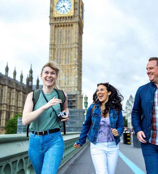Långbenta vuxna kaukasiska vänner har roligt medan de utforskar Londons landmärken. De går förbi Palace of Westminster. De tittar alla på varandra medan de skrattar och rusar genom staden. I bakgrunden finns Elizabeth Tower. De bär ryggsäckar och en kamera.