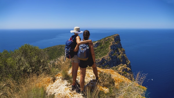 Två kvinnliga vandrare på bergstoppen med utsikt över Medelhavet.