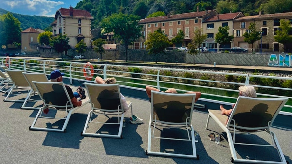 Några gäster i solstolar på soldäck som överblickar fransk by.