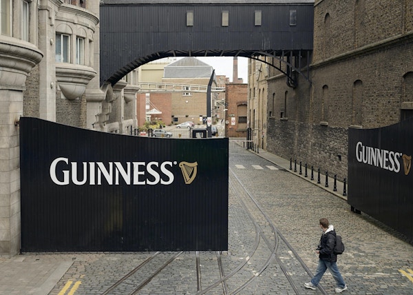 Dublin Irland - 5 maj 2012: En man som går förbi stora ingångsportar till St. James's Gate-bryggeriet i Dublin, där Guinness har gjorts sedan 1759.