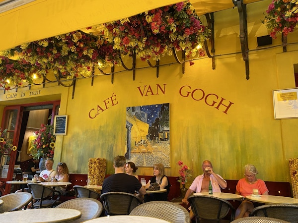 Ett café: Gul vägg målad med platsens titel och det sitter flera personer och tar en drink