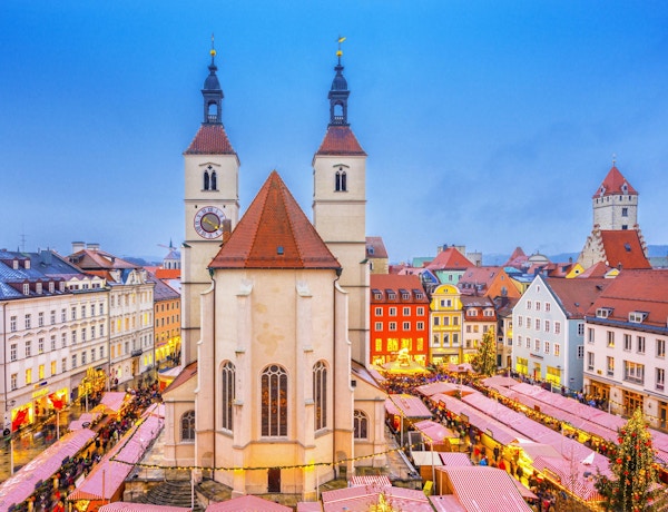 Förhöjd utsikt över Regensburgs julmarknad med mat- och juldekorationsbås runt den 500 år gamla Neupfarr-kyrkan och vackra hus.