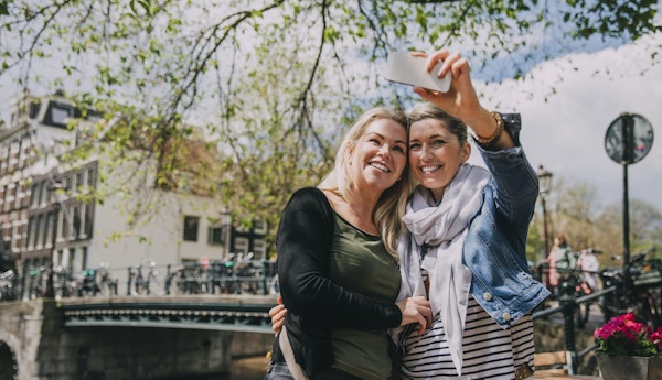Två kvinnor i Amsterdam som tar en selfie vid floden.