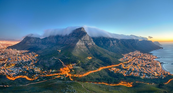 Table Mountain covered by its typical cloud table cloth and the twelve Apostles. Below on the left you can see Cape Town and the beautiful Camps Bay on the right. Taken right after sunset.