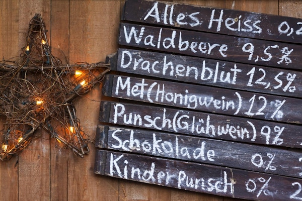 "Drickmeny med alkoholhaltiga och alkoholfria drycker på en tysk julmarknad, kritad på tavlor av träplattor. Drycker är, med deras alkoholhalt, topp till botten, Alles Heis, en varm kryddig dryck, Waldbeere, en vild, skogsfruktdrink , Drachenblut, en Herby Beer, Met Honigwein, ett honungsvin, Punsch Gluhwein, ett varmt glögg, Schokolade, varm choklad, Kinder Punsch, en Multi Fruit Punch med kryddor, för barn "