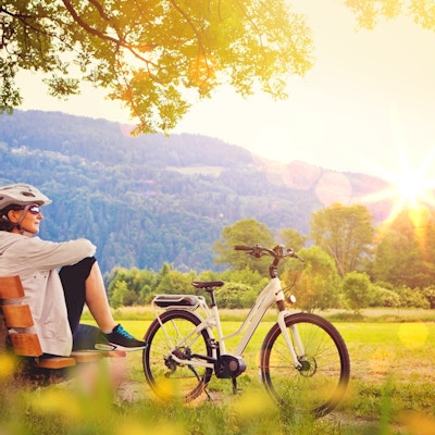 Cyklist sitter på en bänk i vackert landskap med solnedgången bakom kullen.