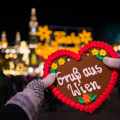 hand med handskar som håller pepparkakahjärta av pepparkakor på julmarknaden i Wien som skickar hälsningar från Österrike