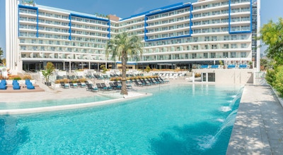 Pool och soldäck med solstolar och plamträd, hotellbyggnaden, blå himmel, L'Azure Hotel, Lloret de Mar, Spanien