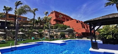 Pool med solstolar och palmer, hotellet och glå himmel, Manilva Green, Marbella, Spanien