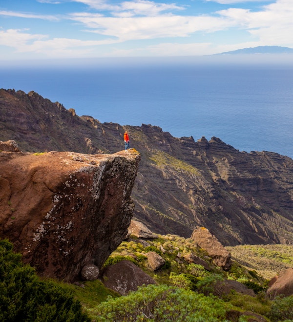 Hög vinkelvy av person som står på kanten av klippan med utsikt över blått hav