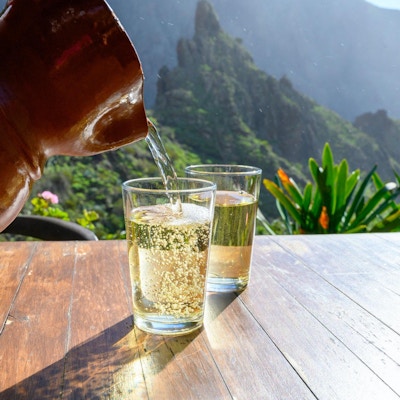 Man häller vitt vin från lerkanna i glas på terrassen med utsikt över gröna landskap i den lilla bergsbyn Masca på Teneriffa, Spanien i solig dag